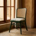Goa green cane dining chair beside a window in a rustic interior