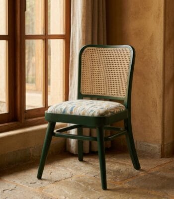 Goa green cane dining chair beside a window in a rustic interior