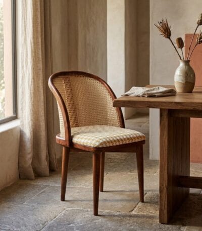 Kaen cane dining chair at a wooden dining table by a window